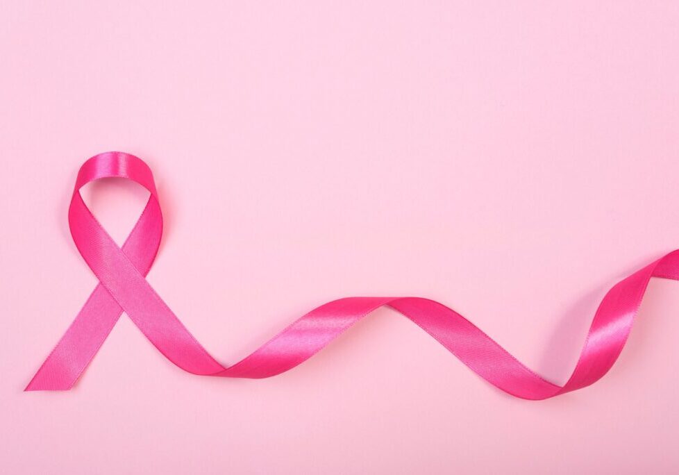 Pink ribbon symbolizing breast cancer awareness on a soft pink background.